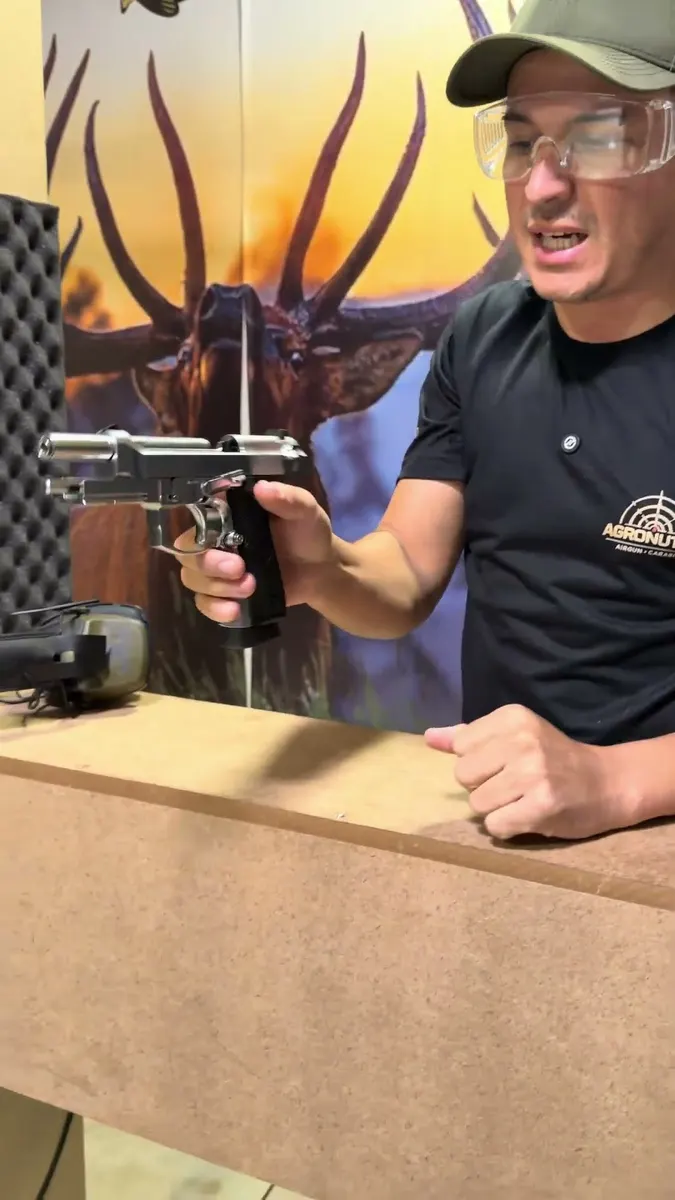 Atendente mostrando uma pistola de pressão no balcão do estande